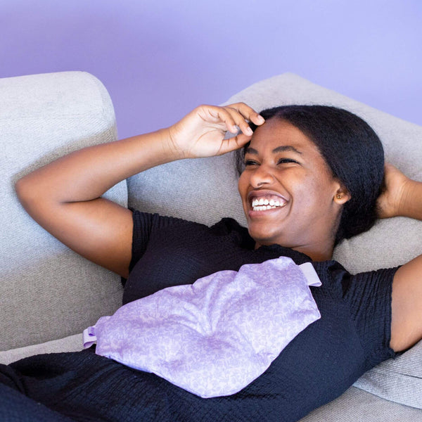 Woman lying on a couch with a purple heating pad on her stomach